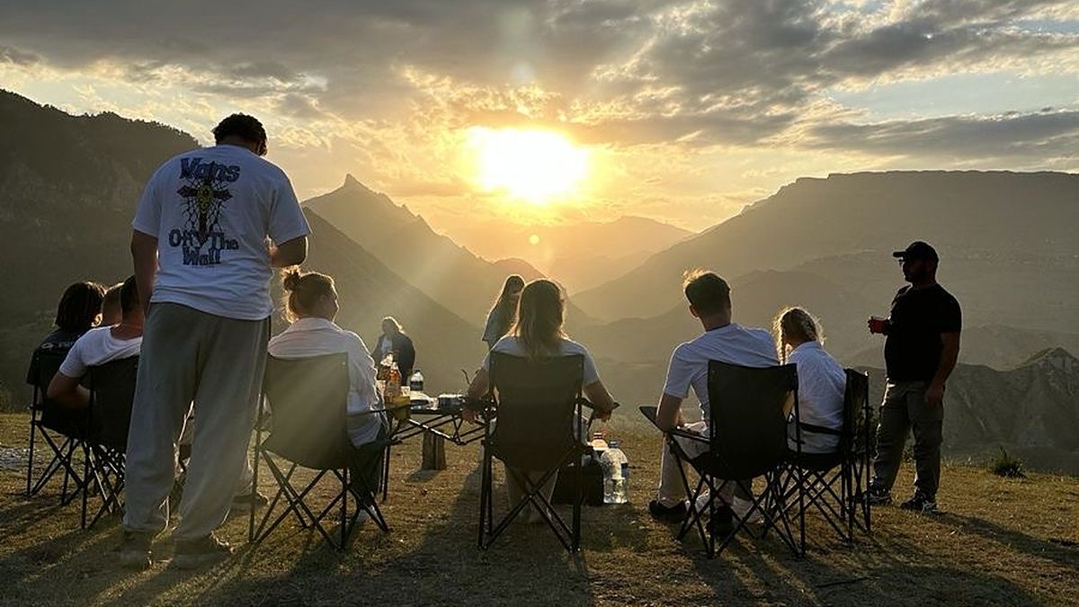 A group of friends sitting on camp chairs on a hilltop at sunset