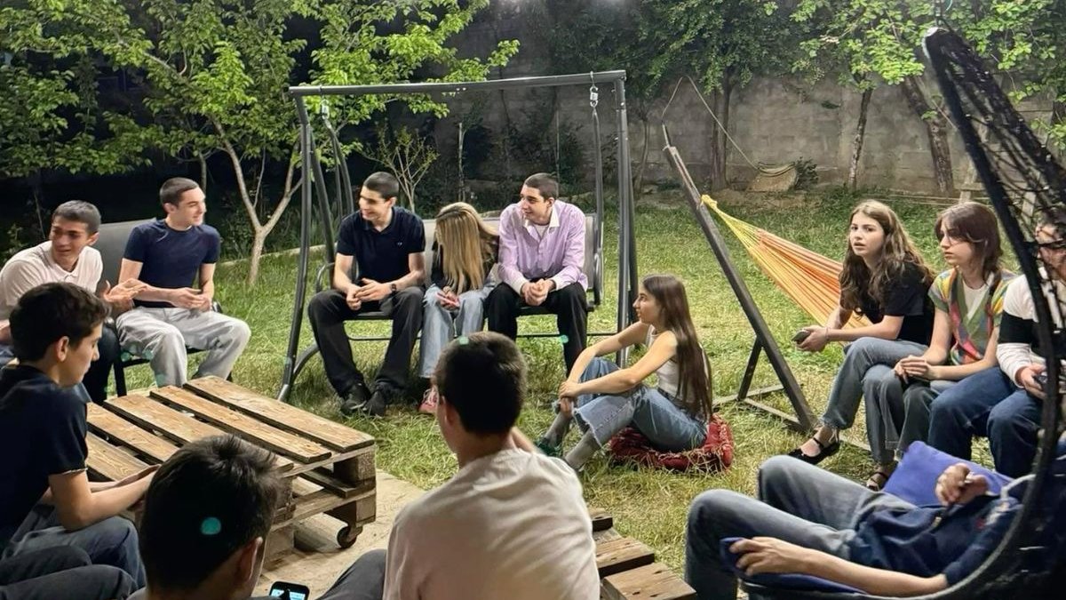A group of young people sitting and talking in a garden under string lights