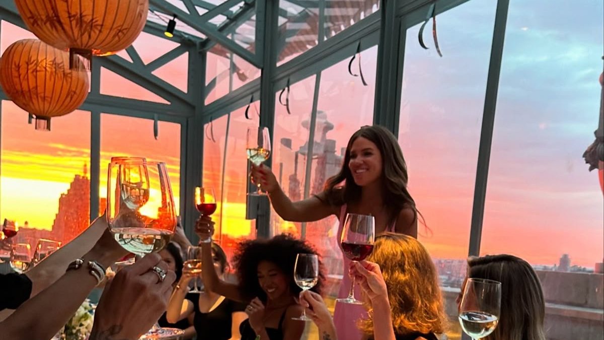 A host raising a toast to guests at a rooftop dinner at sunset
