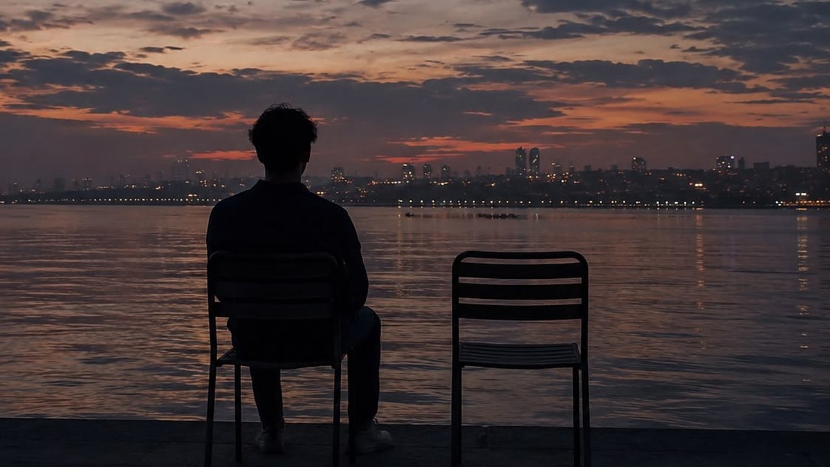 A man sitting alone by the water at dusk next to an empty chair
